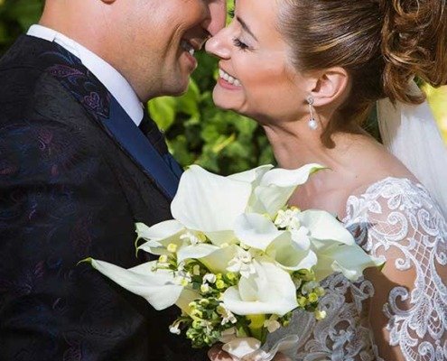 Novio abrazando a la novia sonriente sujetando su ramo de calas