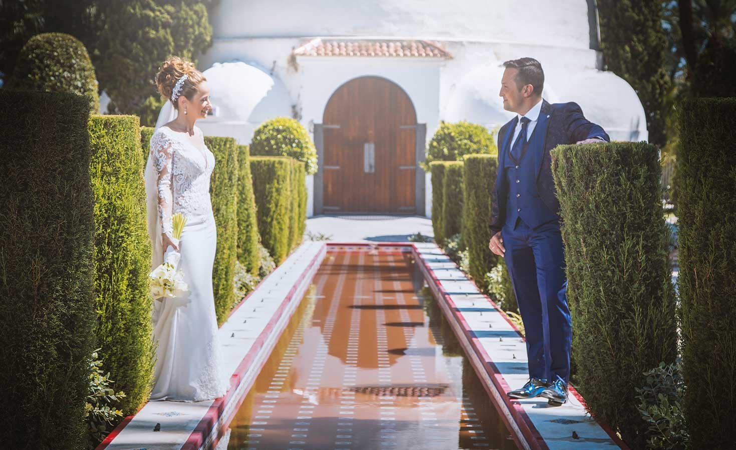 Novios paseando junto a una fuente alargada en jardines clásicos de Alicante