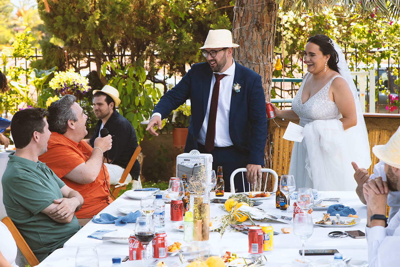 Novios e invitados sentados compartiendo risas y comida en una mesa decorada al aire libre en la finca.