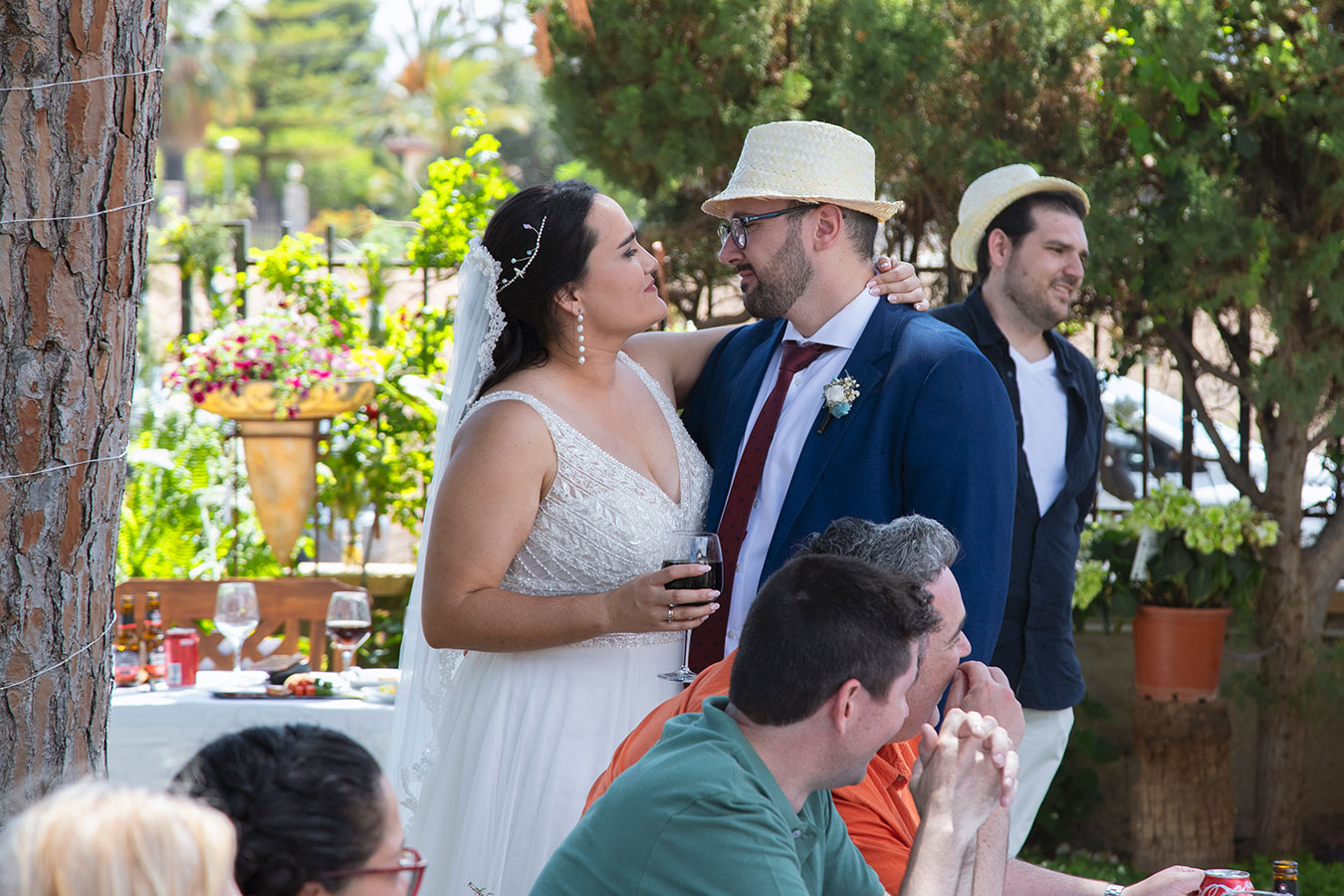 Los novios sonriendo y brindando con sus bebidas junto a los invitados durante la celebración del banquete.