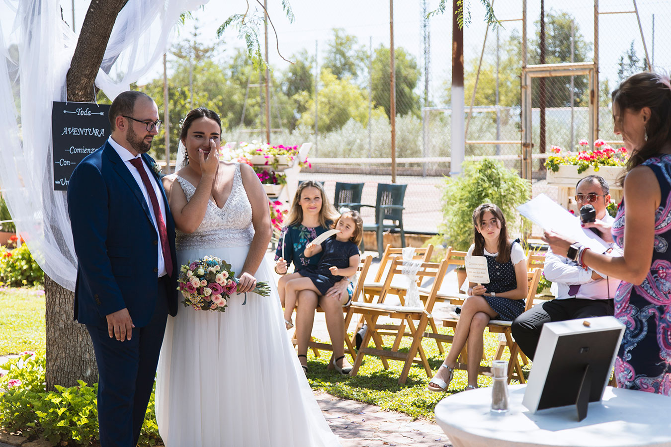Vista del altar, los novios, la oficiante y los invitados sentados rodeados de árboles durante la boda civil en finca.