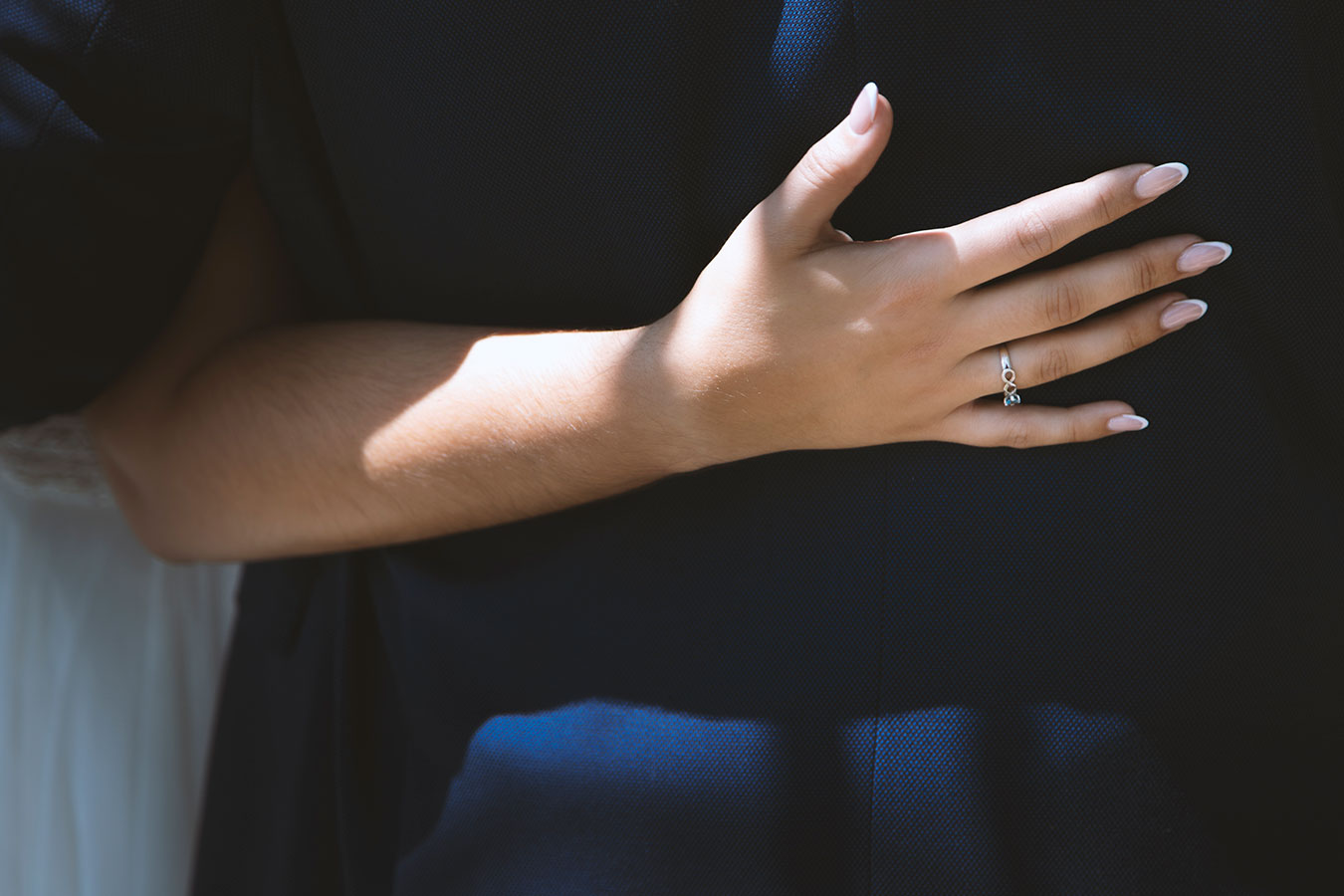 Primer plano de la mano de la novia mostrando su anillo sobre el traje de novio de color azul oscuro.