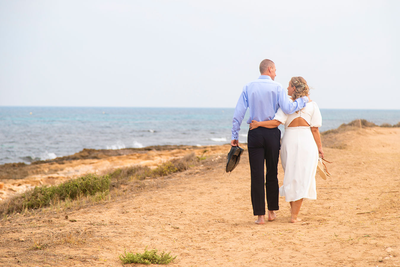 Vista trasera de los novios paseando por el sendero natural junto al mar en Cala Ferris, Torrevieja.