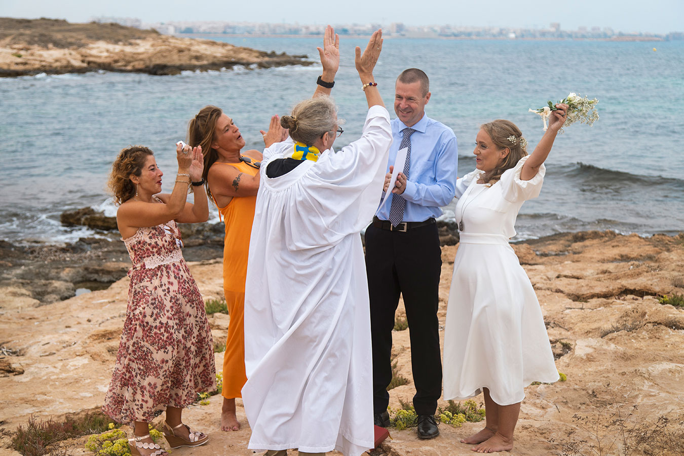 Novios e invitados alzando los brazos festejando el final de la ceremonia en Cala Ferris, Torrevieja.