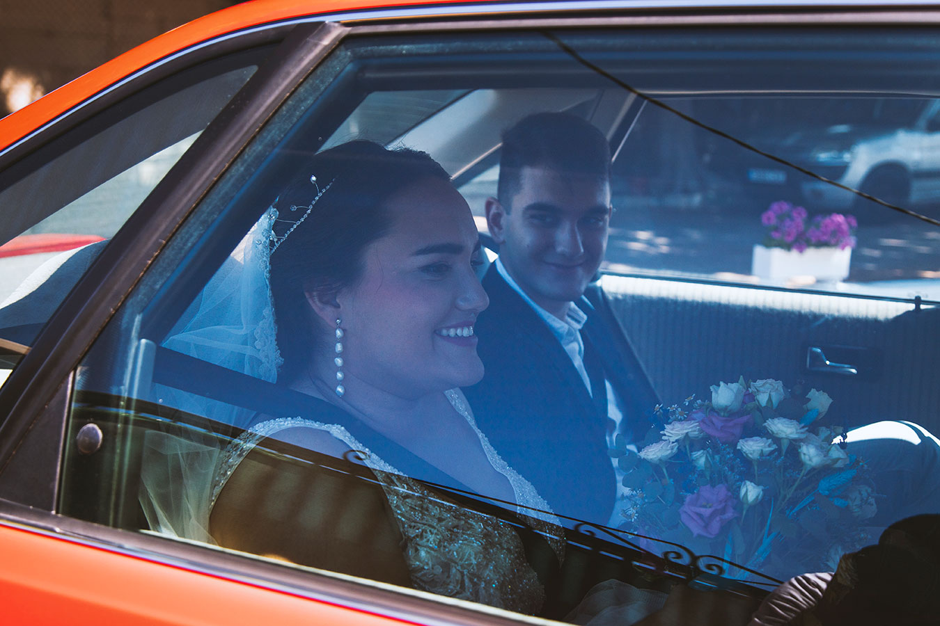 Retrato documental de los novios sonriendo a través de la ventanilla de un coche clásico rojo a su llegada a la boda.