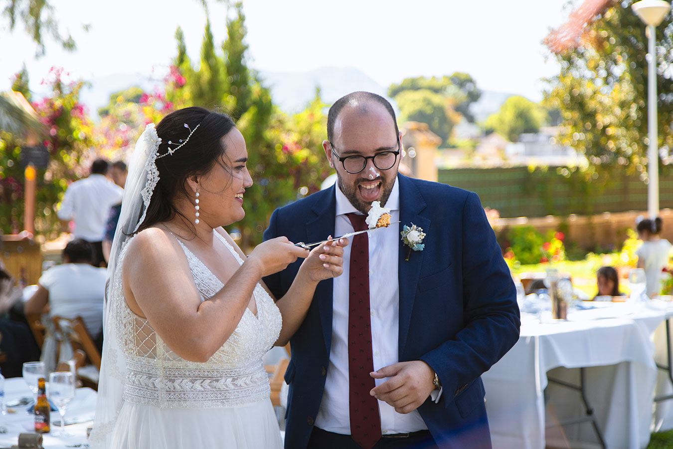 Fotografía documental divertida de la novia y el novio dándose a probar un trozo de tarta con la cuchara.