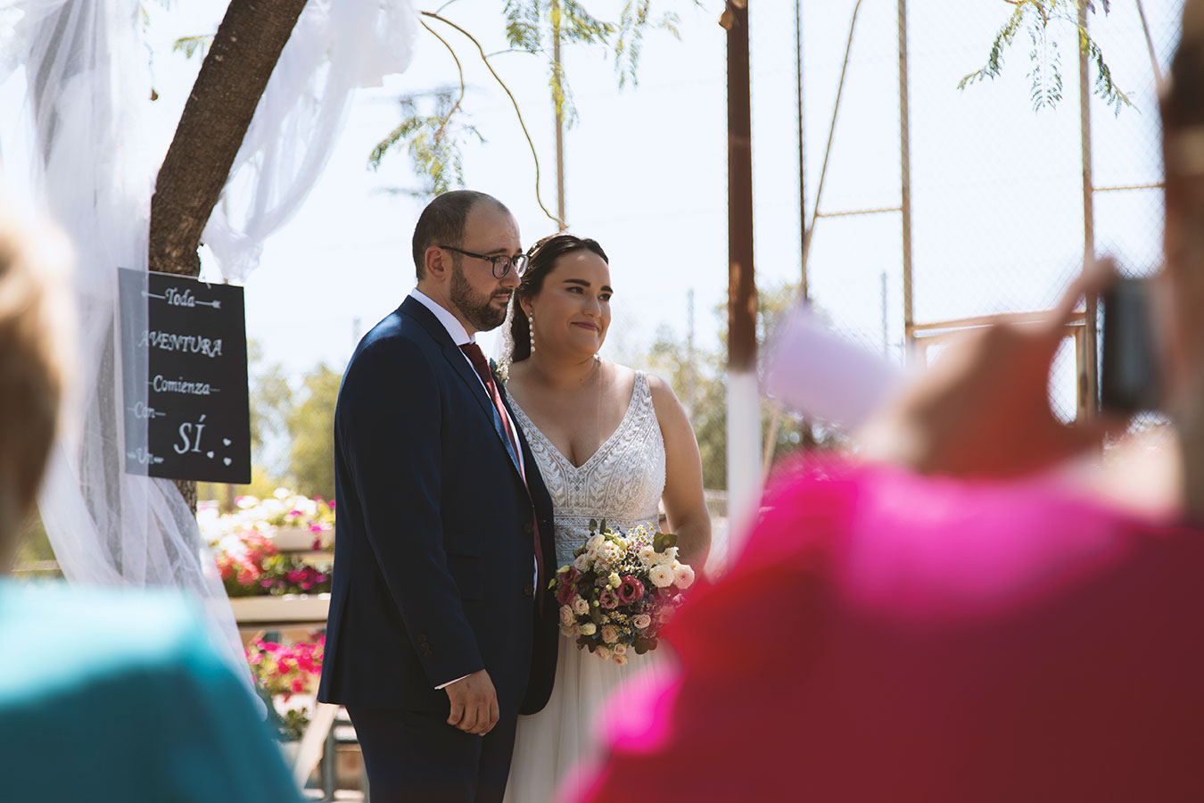 Invitada fotografiando a los novios en el altar desde su asiento durante la boda al aire libre.