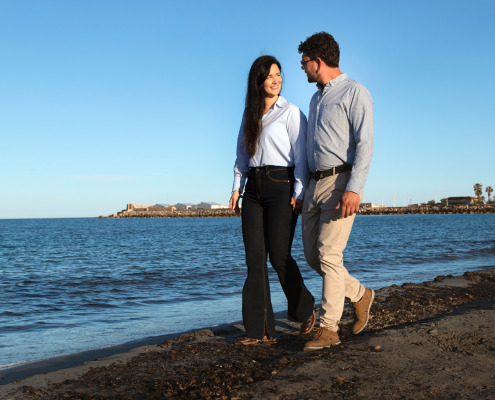 Pareja paseando de la mano por la orilla de la playa durante un reportaje fotográfico de preboda.