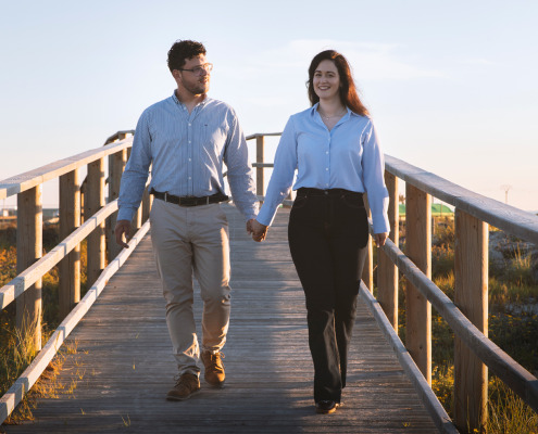 Novios caminando juntos sobre una pasarela o puente de madera en un entorno de naturaleza abierta.