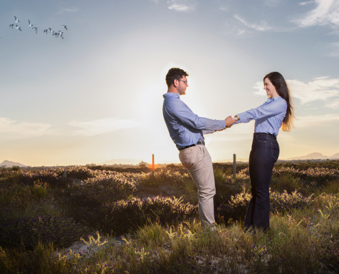 Silueta de pareja de novios de pie bajo la luz cálida del atardecer en un paraje natural.